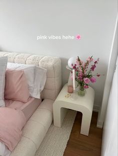 a white couch with pink pillows on it and a vase full of flowers in the corner