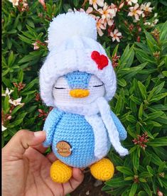 a small crocheted penguin with a red bow on its head is in front of some flowers