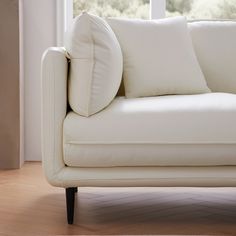 a white couch sitting in front of a window next to a wooden floor and wall