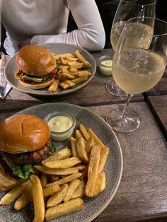 two plates with hamburgers and french fries on them next to a glass of wine