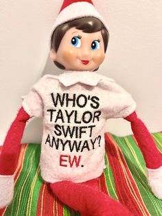 the elf is wearing a t - shirt that says who's taylor swift anyway?