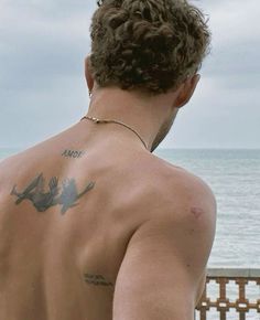 a man with tattoos on his back looking at the ocean