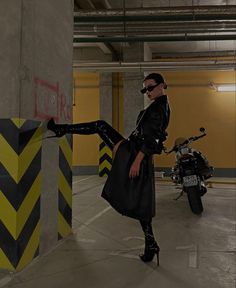 a woman dressed in black is leaning against a pole and posing for the camera with her legs spread out