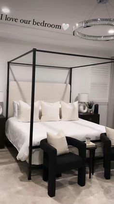 a white bed sitting in a bedroom next to two black chairs and a chandelier