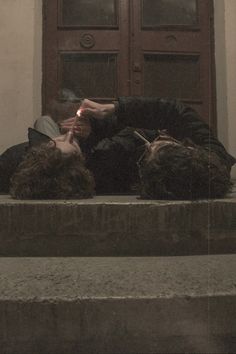 two people laying down on the steps in front of a door with their eyes closed