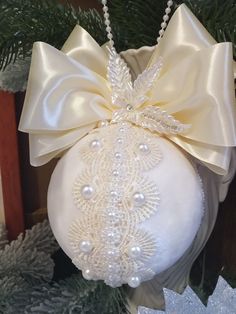 a white ornament hanging from a christmas tree with pearls and bows on it