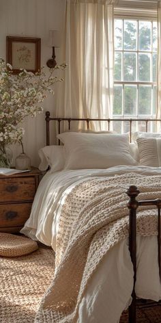 a bed sitting under a window next to a dresser with flowers on top of it