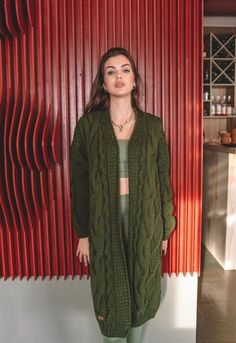 a woman standing in front of a red wall wearing a green sweater and leggings