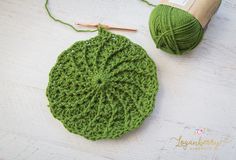 a green crochet pot holder with yarn next to it and a ball of thread