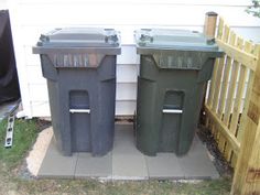 two trash cans sitting next to each other in front of a fenced off area