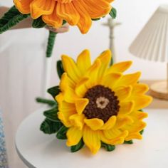 two fake sunflowers sitting on top of a white table next to a lamp