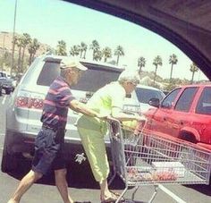 an older man pushing a shopping cart in a parking lot next to another old man