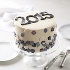 a white cake decorated with black and silver confetti on a glass plate next to utensils