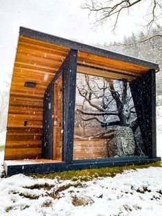 a small wooden structure sitting on top of a snow covered field next to a tree