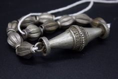 Antique, authentic and used necklace with metal beads from South Nepal, Terai Area. These Necklaces have been used by the Tribal Village Women ( Rana Tharu Tribe) as adornment. Ten antiques matched tribal silver (silver alloy) beads of collared shape and a traditional tribal silver pendant of biconical shape. Collectible and useful as jewelry supplies. Average beads measures/wt: 21 x 12 mm/9.6g Pendant measures/wt: 66.3 x 23.2 mm/28.1g Total Weight: 124 grams. Origin: Nepal Silver Beaded Temple Necklace For Festivals, Festival Silver Beaded Temple Necklace, Vintage Silver Temple Necklace For Ceremonial Occasions, Traditional Silver Beaded Temple Necklace, Handmade Silver Temple Jewelry Beads, Handmade Silver Temple Necklace With Round Beads, Silver Beaded Temple Jewelry Necklace, Traditional Polished Beads Necklaces For Rituals, Traditional Necklaces With Polished Beads For Rituals