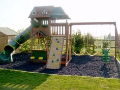 a wooden swing set with a green slide and climbing frame in the grass next to it