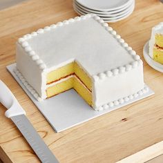 a yellow cake sitting on top of a wooden cutting board next to plates and knives