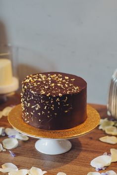 a chocolate cake with gold sprinkles sitting on a table next to flowers