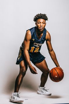 a young man holding a basketball while standing next to a white wall