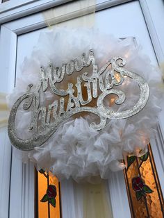 a white wreath with the words merry christmas hanging on it's front entrance door