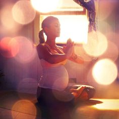 a pregnant woman sitting on the floor in front of a window with her hands together