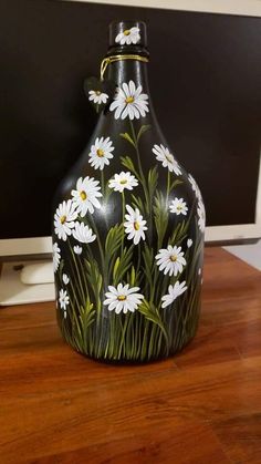 a black vase with white daisies painted on it sitting in front of a computer monitor