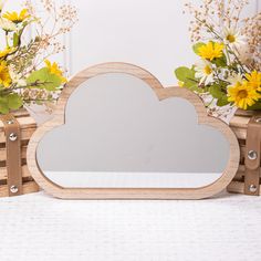 a wooden cloud shaped mirror sitting on top of a table next to vases with flowers