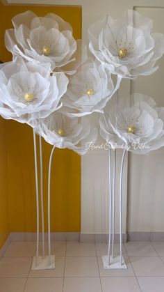 three tall white flowers sitting on top of a tiled floor next to a yellow wall