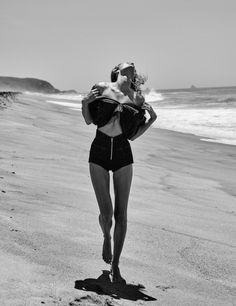 a woman is walking on the beach with her back to the camera while wearing a bathing suit