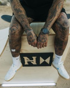 a man sitting on top of a skateboard with tattoos on his arms and legs