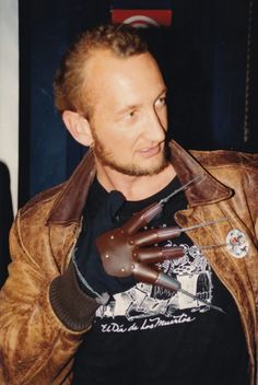 a man in a brown leather jacket is holding his hand up to the camera while wearing gloves