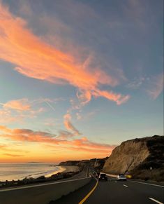 the sun is setting over the ocean as cars drive down the road