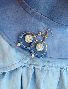 a pair of earrings is hanging from a blue dress with pearls and beads on it