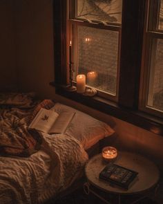 an open book sitting on top of a bed next to a window with candles in it