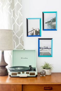 a record player sitting on top of a wooden table next to pictures and a lamp