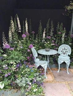 two chairs and table sitting in front of some flowers