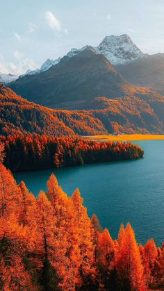 a lake surrounded by mountains and trees with orange leaves on the water's edge