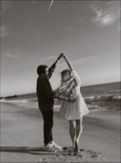 a man and woman standing on top of a beach next to the ocean holding hands