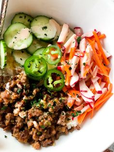 a white bowl filled with meat, vegetables and cucumbers