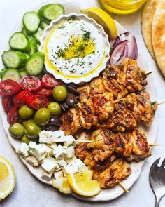 a plate with chicken skewers, olives, tomatoes, cucumbers and pita bread