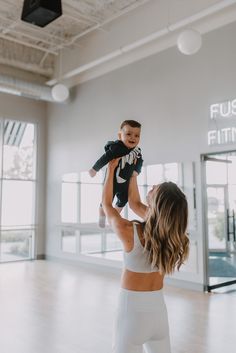 a woman holding a baby up in the air while standing on top of a hard wood floor