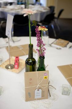 two wine bottles are sitting on a table with flowers in the bottle and a card