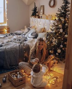 a woman sitting on the floor next to a baby in front of a christmas tree