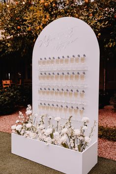 a white display case with flowers and wine glasses on the wall for guests to drink