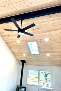 a ceiling fan in a room with wood paneling on the ceiling and windows above it