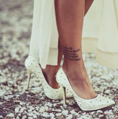 a woman's legs with tattoos on her left leg and white high heeled shoes