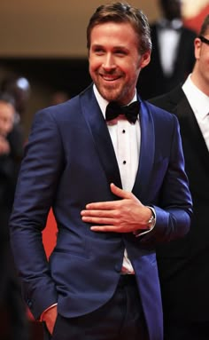 two men in tuxedos standing next to each other on a red carpet and smiling