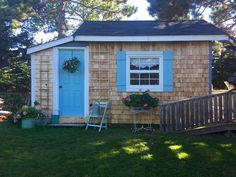 a small wooden house with blue doors and shutters on the outside, next to a deck