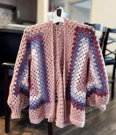 a pink crocheted sweater sitting on top of a wooden table next to a black chair