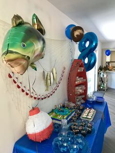 a blue table topped with lots of balloons and other items next to a fish balloon